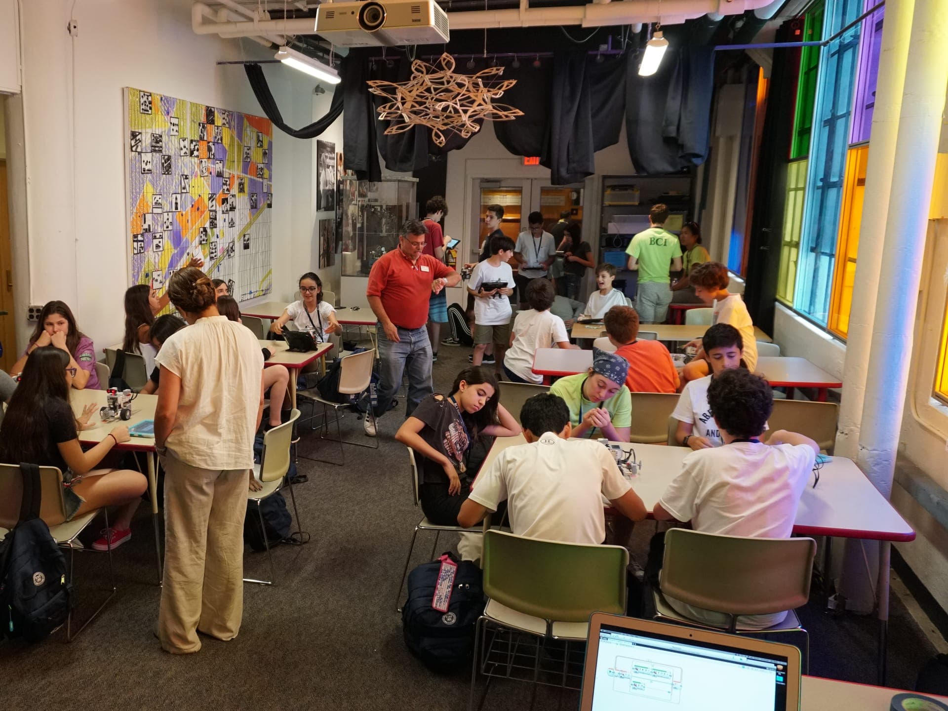 Workshop room in session, with teams at their tables and educators following the work.