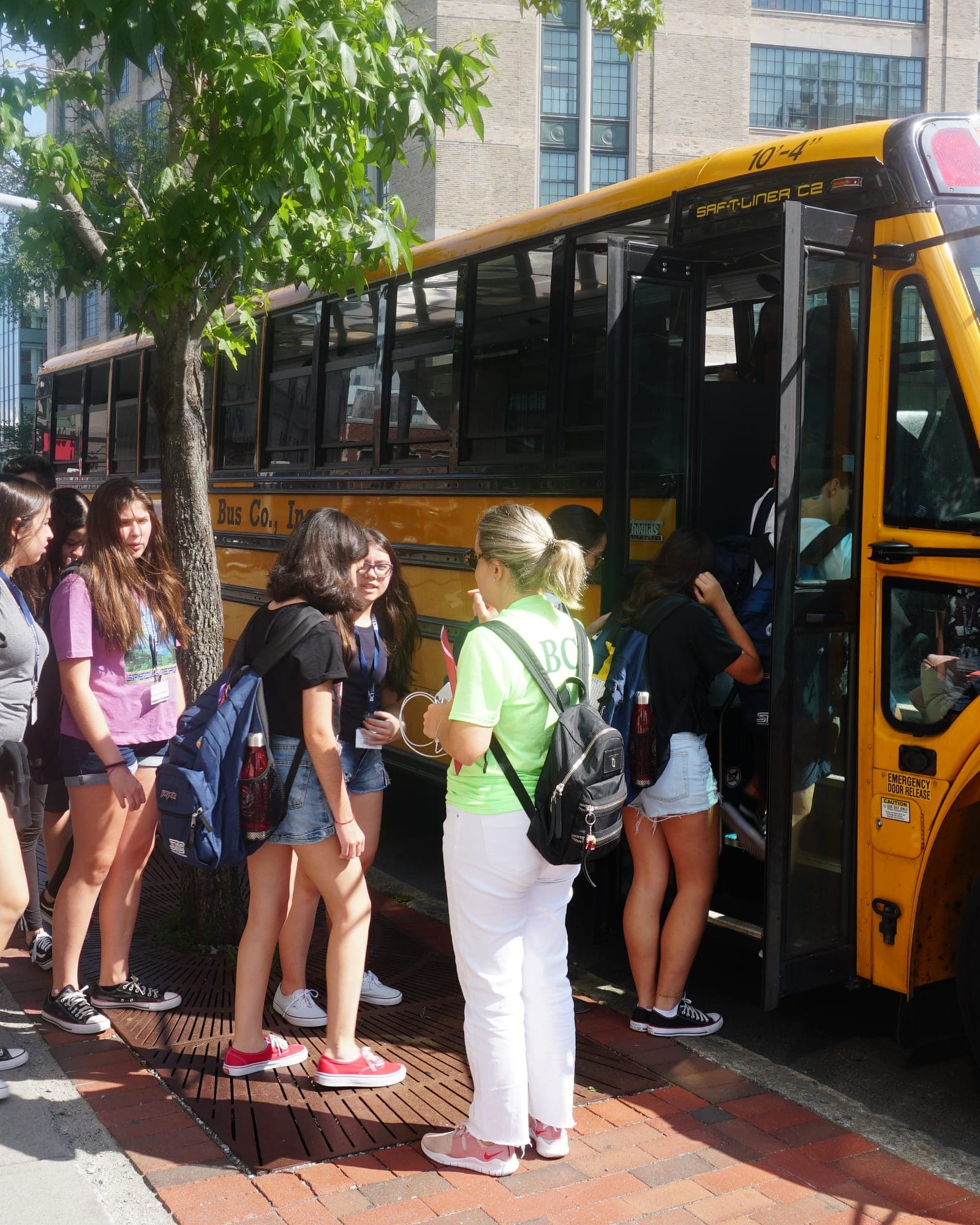 Group boarding the classic yellow school bus while a BCI monitor in the green program shirt keeps count at the door.