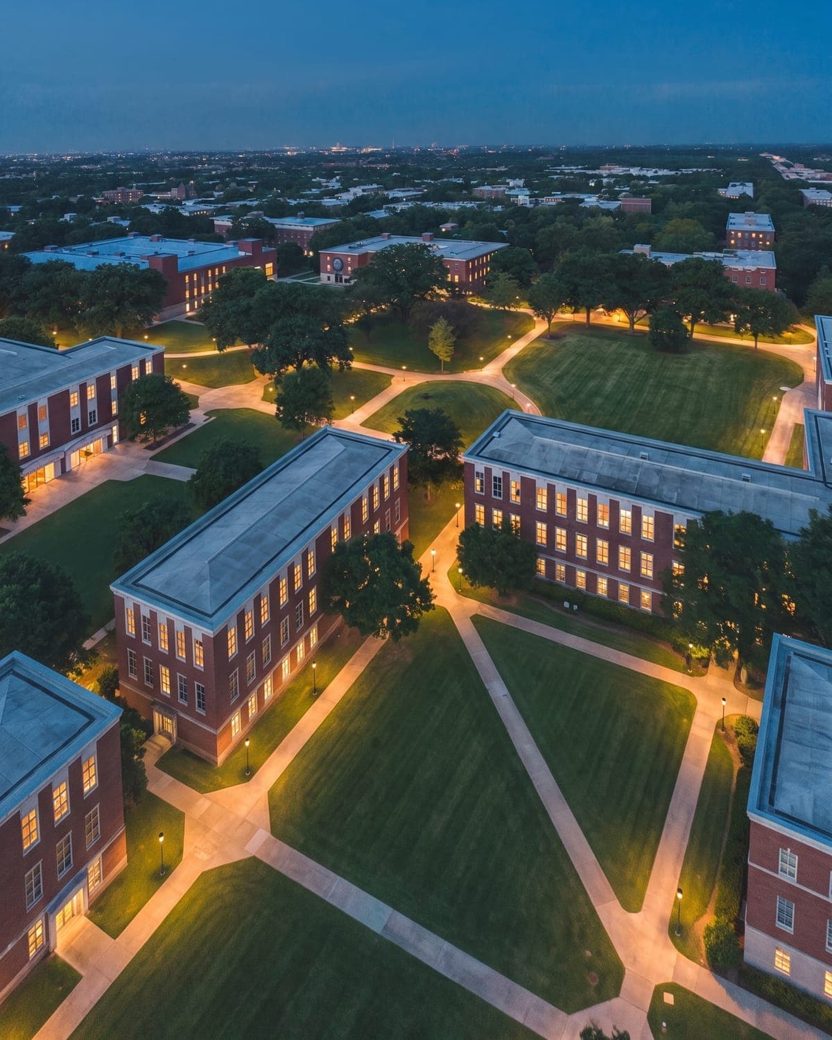 Illustrative aerial image of a university quad at nightfall, gold-lit pathways crossing the lawn between brick buildings.