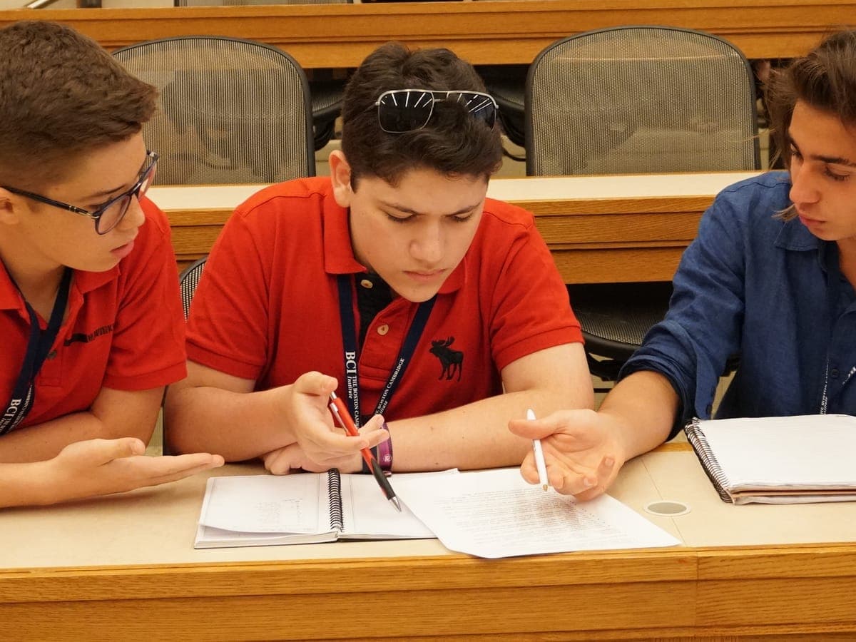 Three participants leaning over a notebook and an annotated handout, pens in hand.