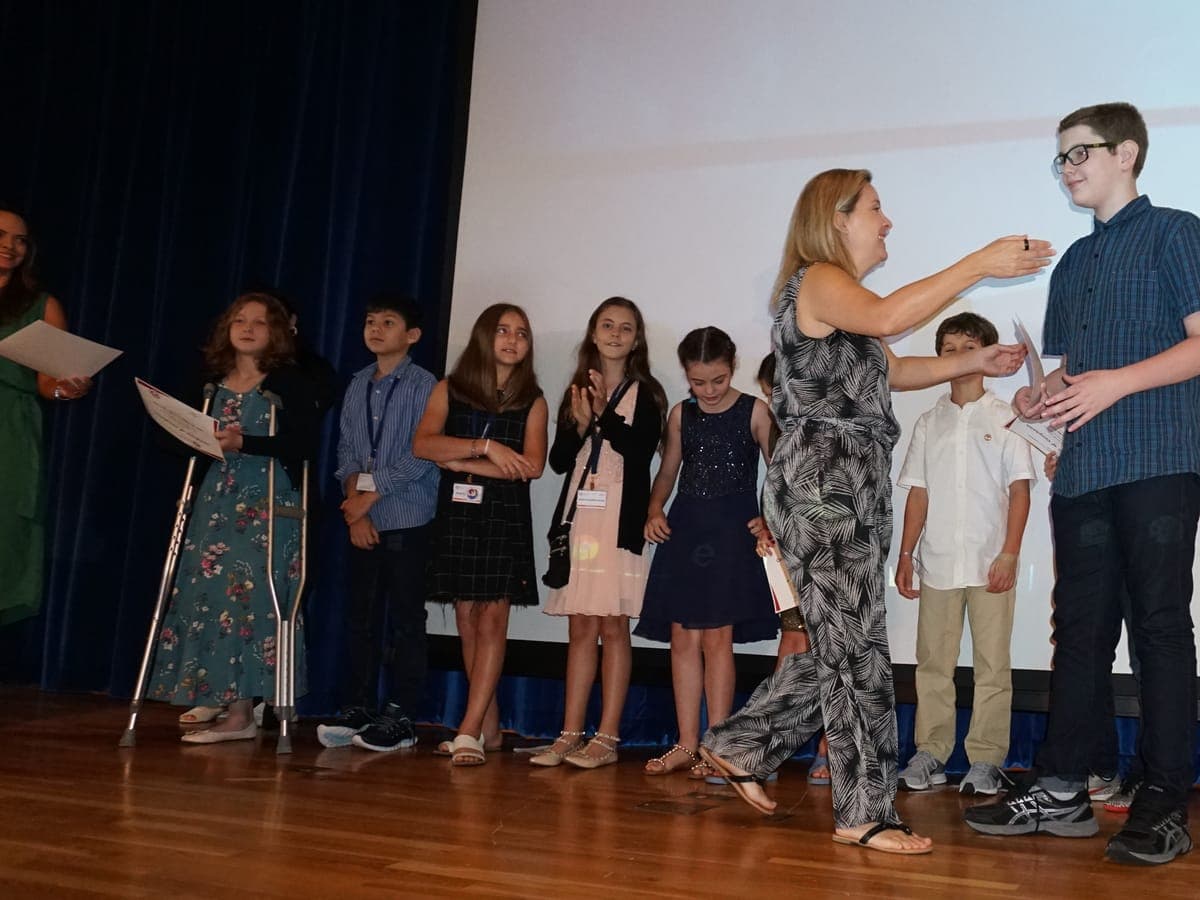A certificate passing from hand to hand on stage, the line of participants waiting their turn.