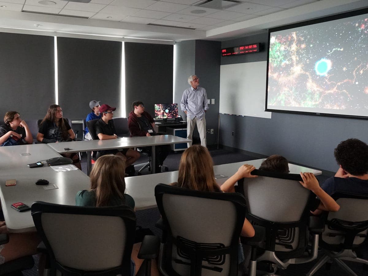 A specialist talking with the group around the meeting table, a scientific image projected behind him.