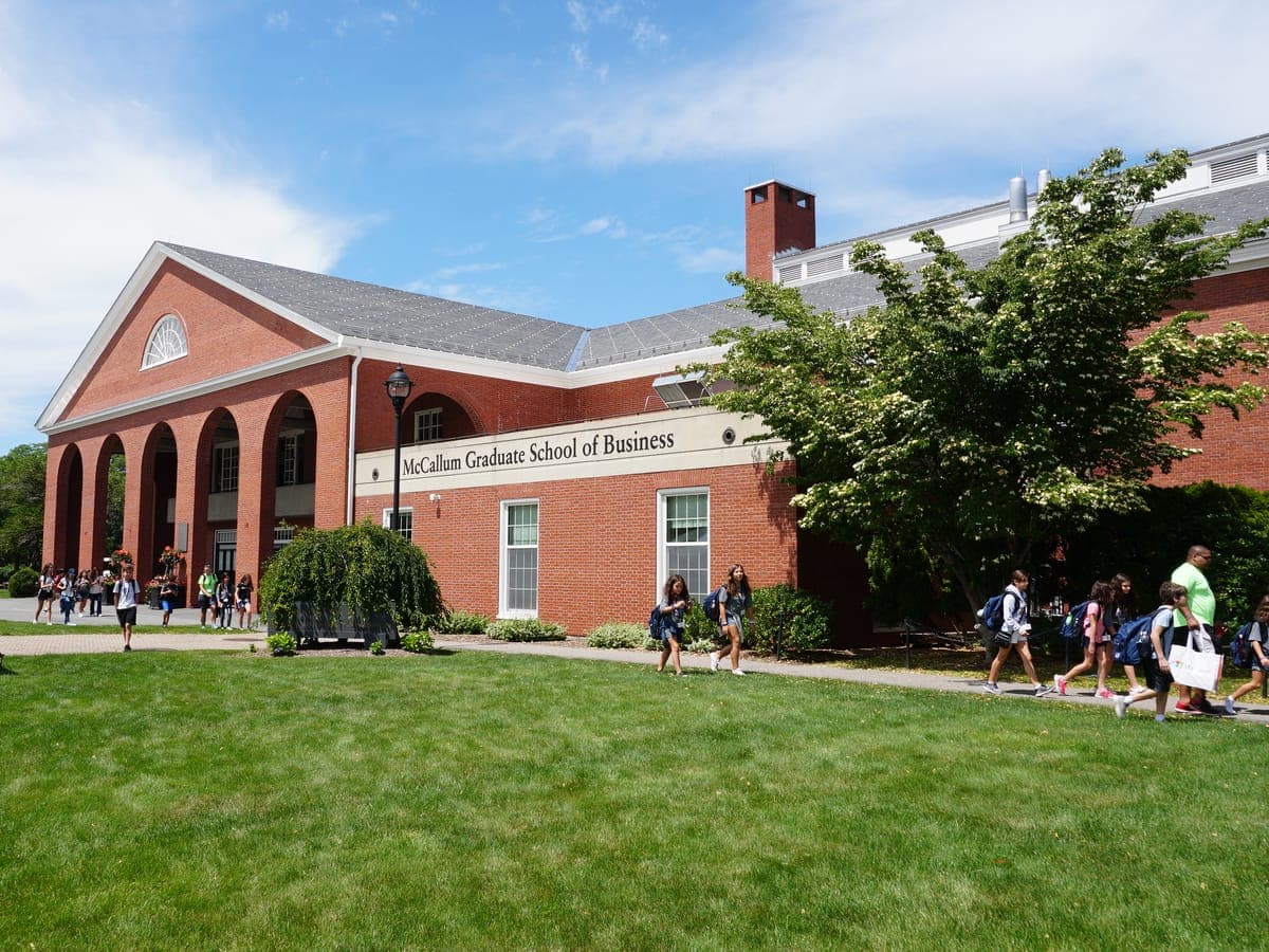 Participants walking across campus in front of the arcaded brick building on a sunny morning.
