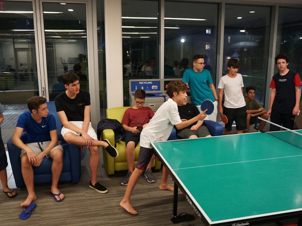 Table tennis game in the residence hall common room at night.